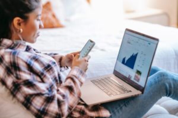 Person analyzing data on laptop while holding smartphone, depicting active business management. #Application maintenance