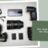 A collection of professional photography equipment arranged on a light background, including a DSLR camera, two lenses, a smartphone, battery packs, and eyeglasses, with a focus on Cameras.